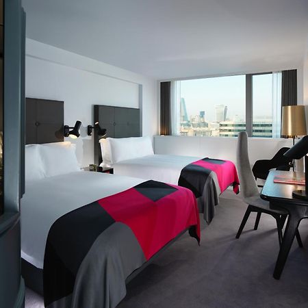 Sea Containers London Hotel Exterior photo The photo shows a modern hotel room featuring two beds with colorful throws in shades of pink and gray. The room has large windows that provide a view of the outside, and there are sleek, contemporary furnishings including a desk and chair. The walls