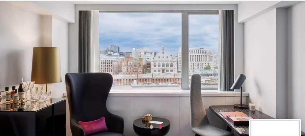 Sea Containers London Hotel Exterior photo The photo shows a modern indoor space, likely a hotel room or office, with large windows offering a view of a cityscape. In the foreground, there are two stylish chairs, one black and one grey, alongside a small round table with a decorative item on 