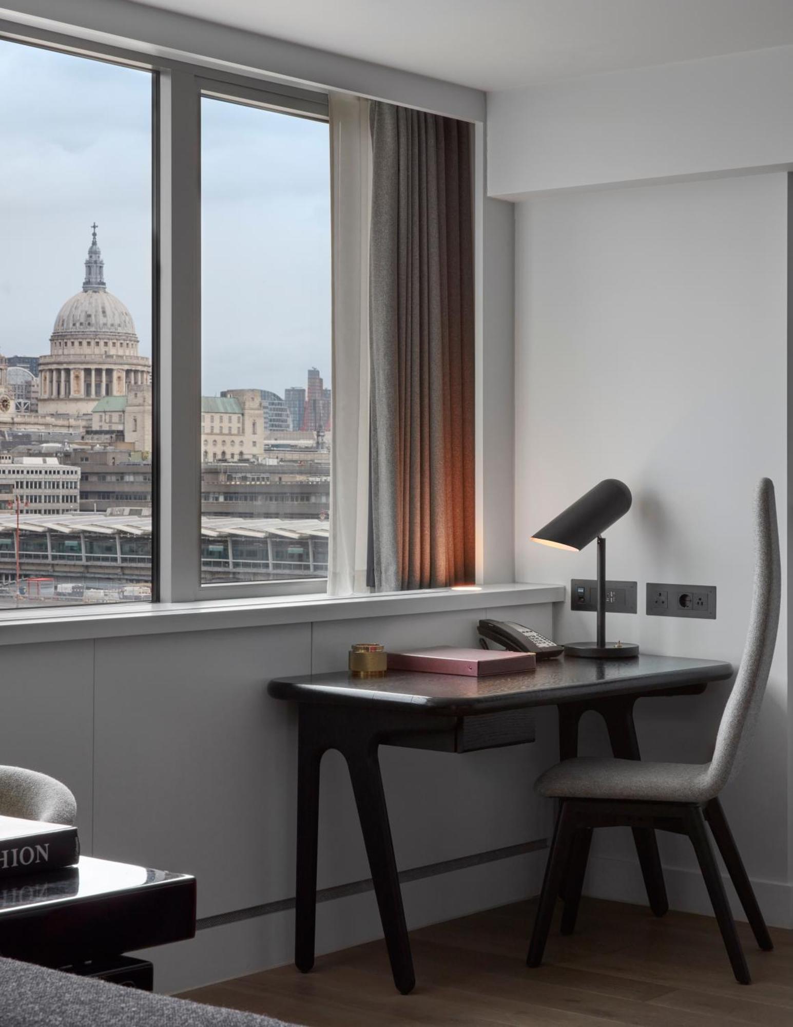 Sea Containers London Hotel Exterior photo The photo shows a modern office space with a view of a cityscape featuring a prominent dome, likely a historic building. There's a sleek desk with a lamp, a phone, and some stationery. The room has large windows allowing natural light to enter, and t