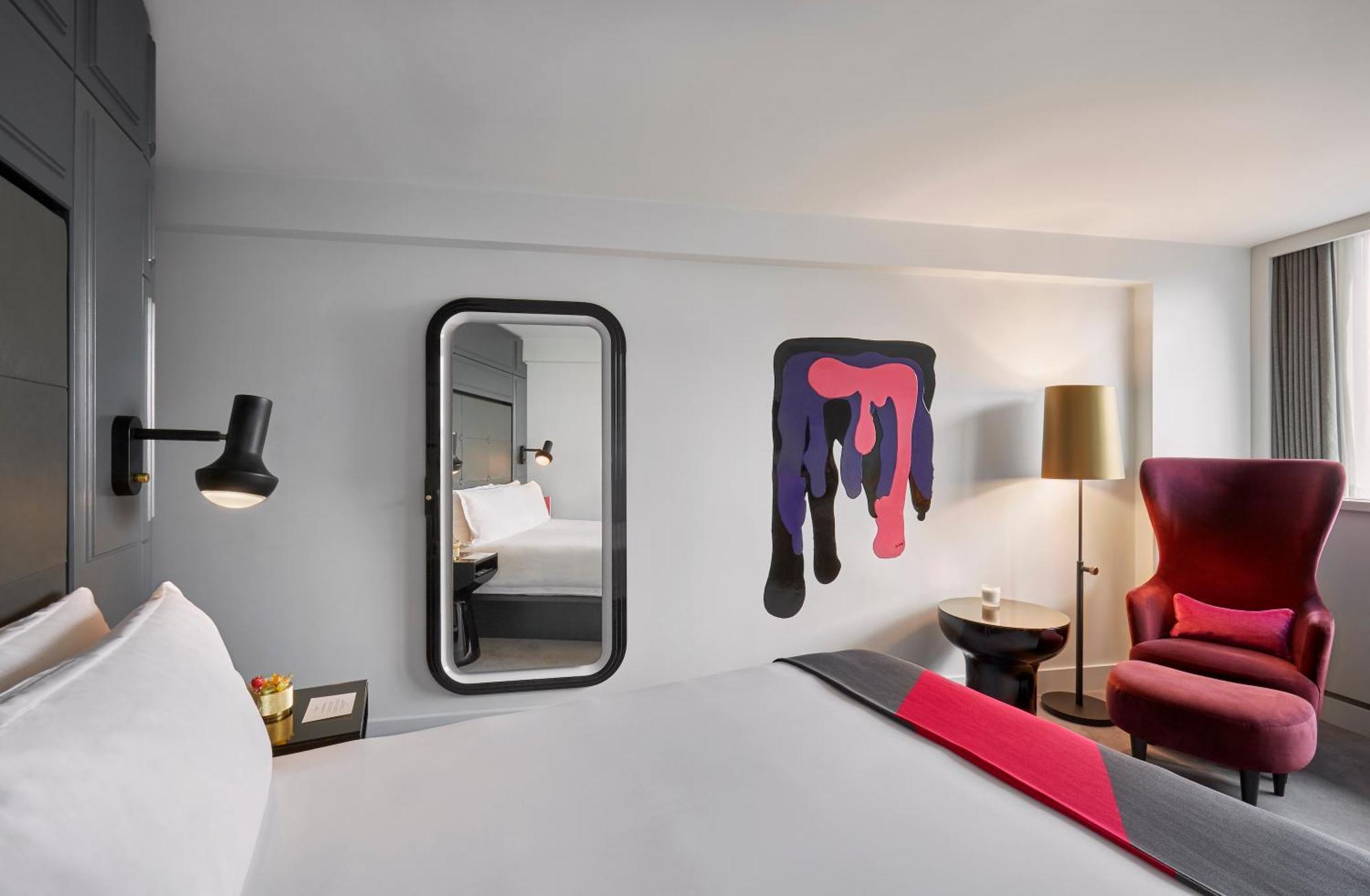 Sea Containers London Hotel Exterior photo The photo shows a modern hotel room with a minimalist design. There is a large bed with white bedding against a light-colored wall. A stylish mirror is mounted on the wall next to the bed, and there's a decorative piece of artwork featuring bold colo