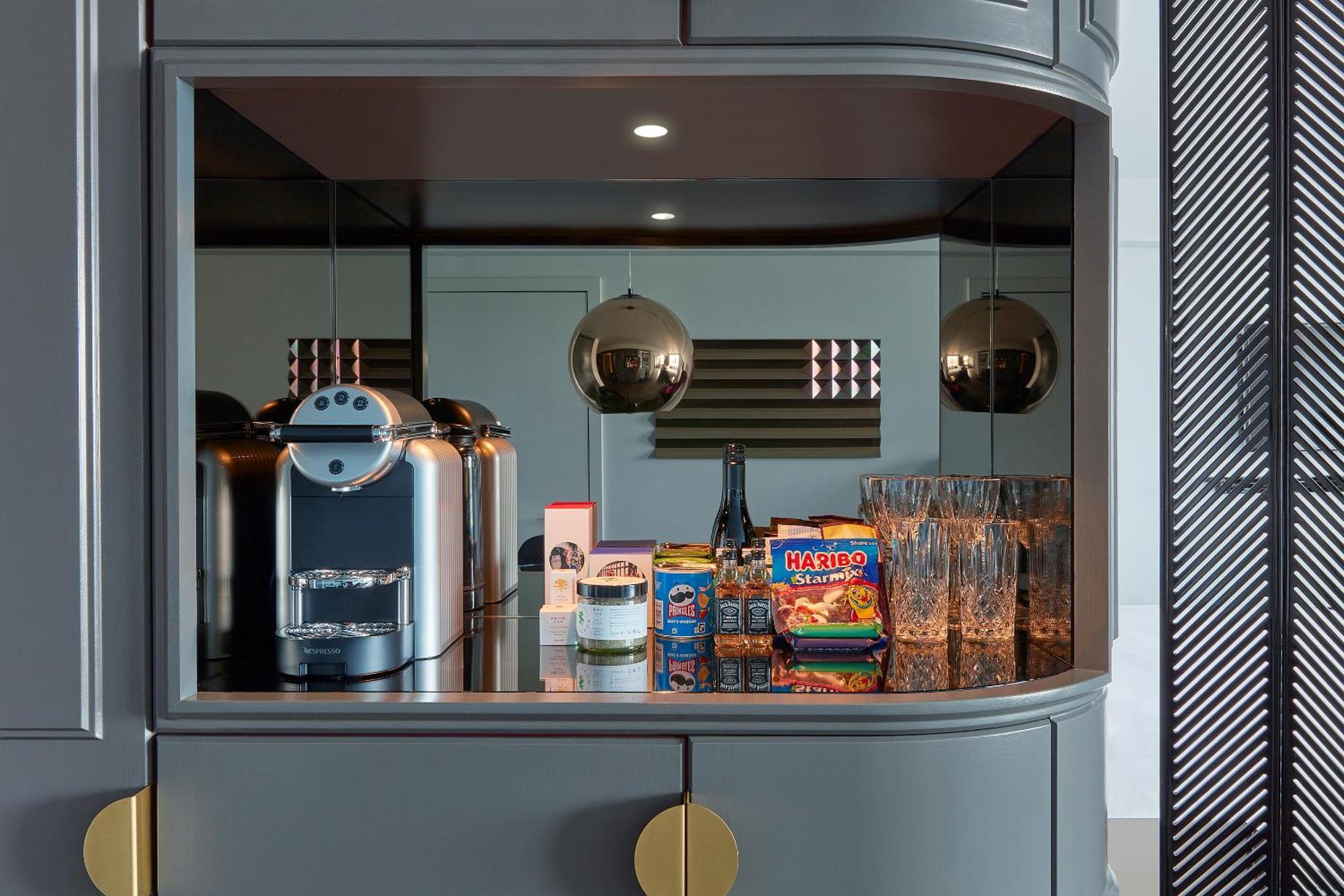 Sea Containers London Hotel Exterior photo The photo displays a modern kitchen nook with a sleek design. It features a coffee machine on the left, placed on a dark countertop. Next to it, there are several glass drinking glasses arranged neatly. Prominently displayed is a colorful box of snac