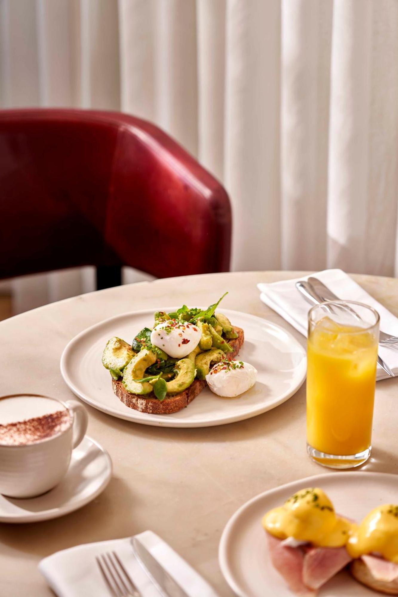 Sea Containers London Hotel Exterior photo The photo shows a plate of food featuring sliced avocado on toast, topped with poached eggs and garnished with herbs and spices. The toast appears to be whole grain. There's also a glass of orange juice on the side and a cup of coffee, possibly cappu