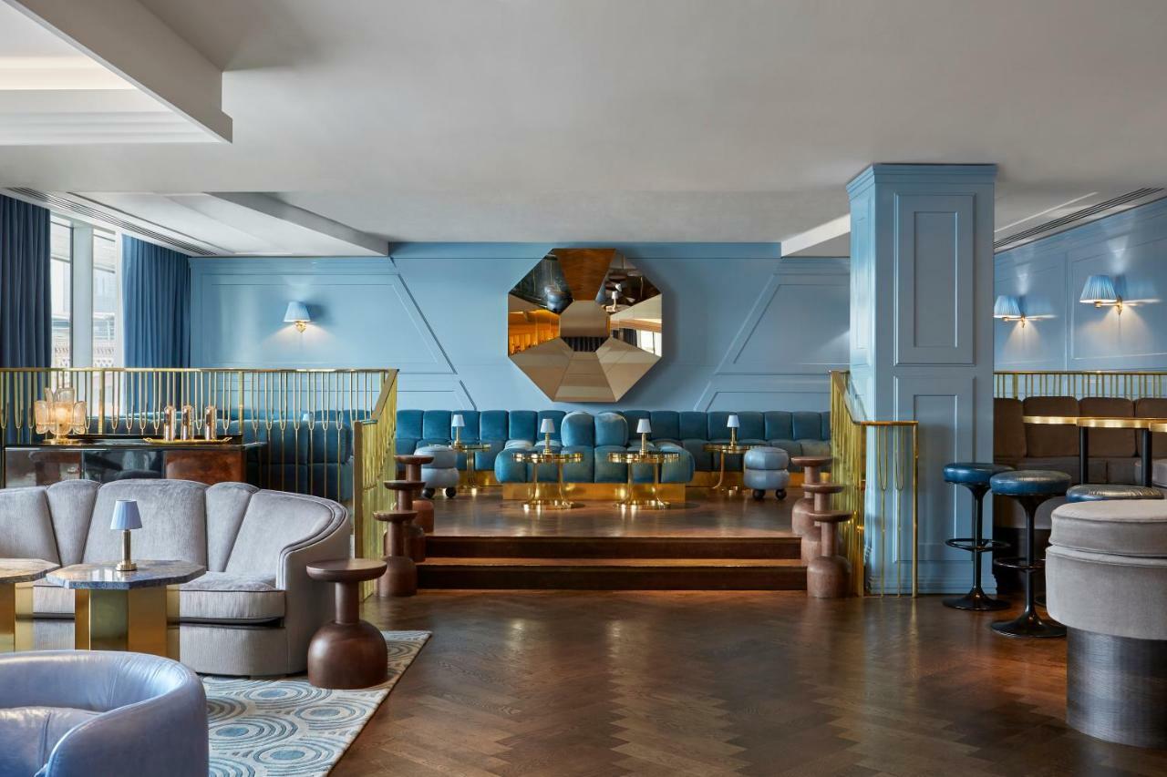 Sea Containers London Hotel Exterior photo The photo shows a stylish and modern interior of a lounge or bar. The space features soft blue walls and various seating options, including plush armchairs and small tables. There is a prominent mirror that's octagonal in shape, adding a decorative e