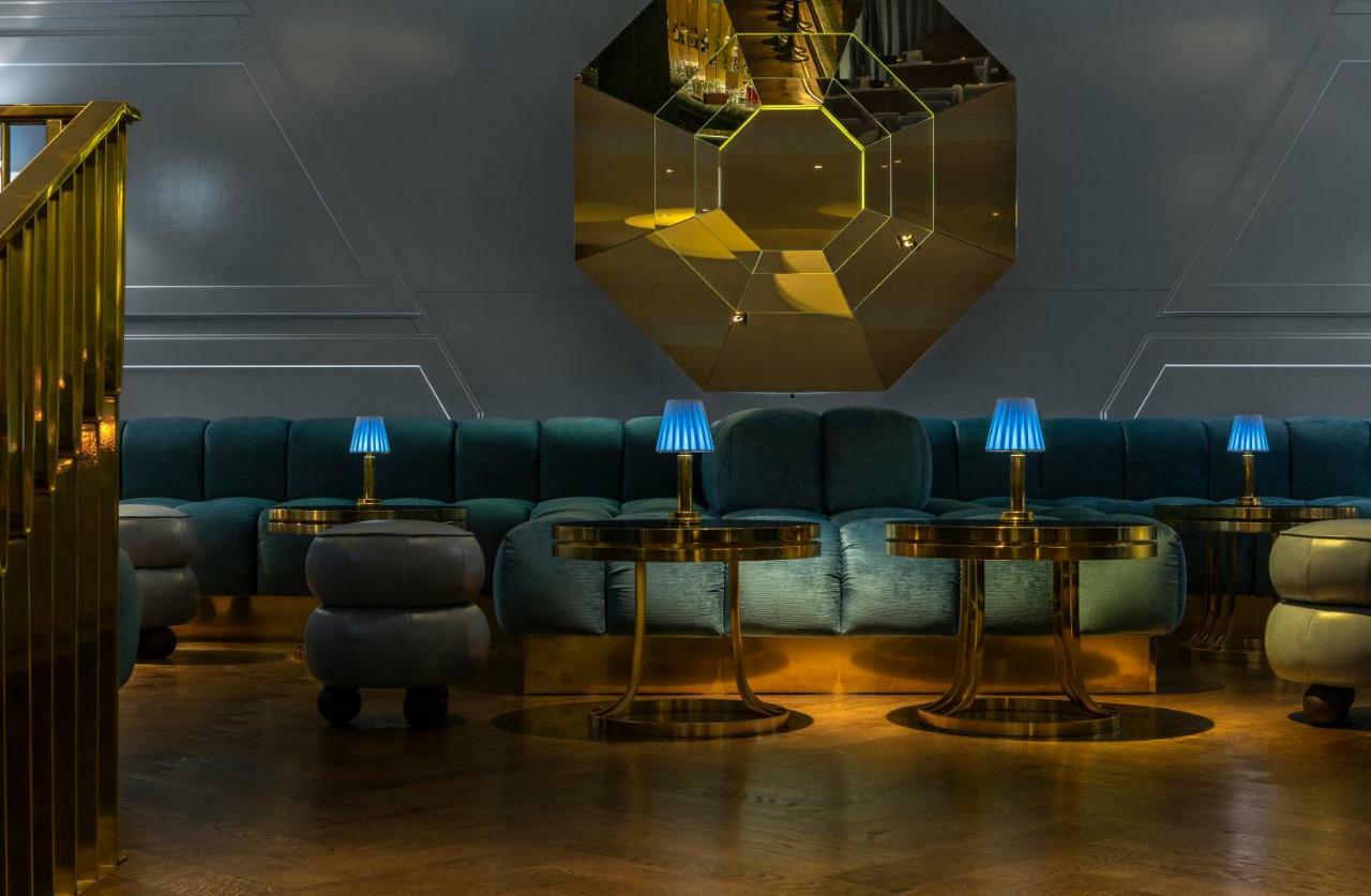 Sea Containers London Hotel Exterior photo The photo showcases a stylish, modern lounge or seating area. It features a curved, plush couch in a soft teal color, complemented by golden accents. There are several circular tables with shiny metallic bases, each topped with small blue lamps that 