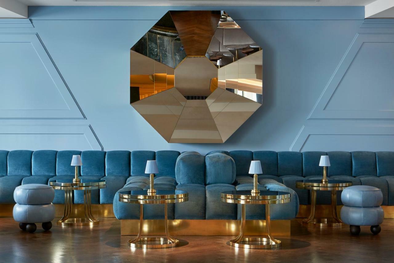 Sea Containers London Hotel Exterior photo The photo depicts a stylish and modern interior space. The focal point is a large, octagonal mirror mounted on the wall, which reflects light and adds depth to the room. In front of the mirror, there is a plush, curved sofa in a soft blue hue. The so