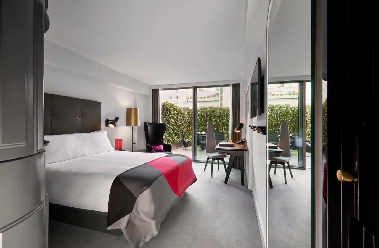 Sea Containers London Hotel Exterior photo The photo shows a modern hotel room featuring a large bed with a minimalist design. The bed is adorned with a colorful bedspread, primarily in shades of gray, white, and pink. There are two large windows that provide natural light and overlook a gree