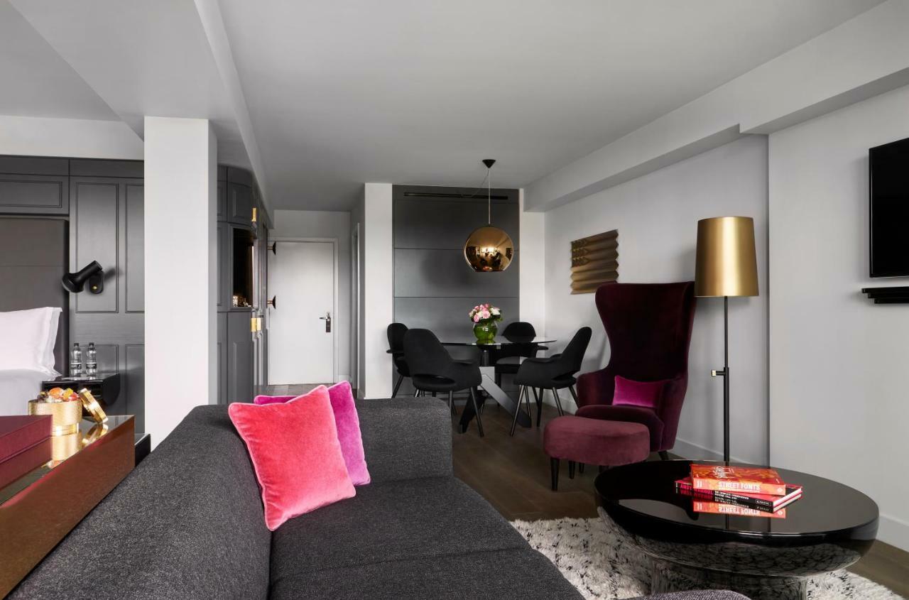 Sea Containers London Hotel Exterior photo The photo shows a modern and stylish living space. There is a gray sofa with two pink cushions in the foreground. In the background, there is a dining area with a round black table and black chairs. A decorative pendant light hangs above the table. T