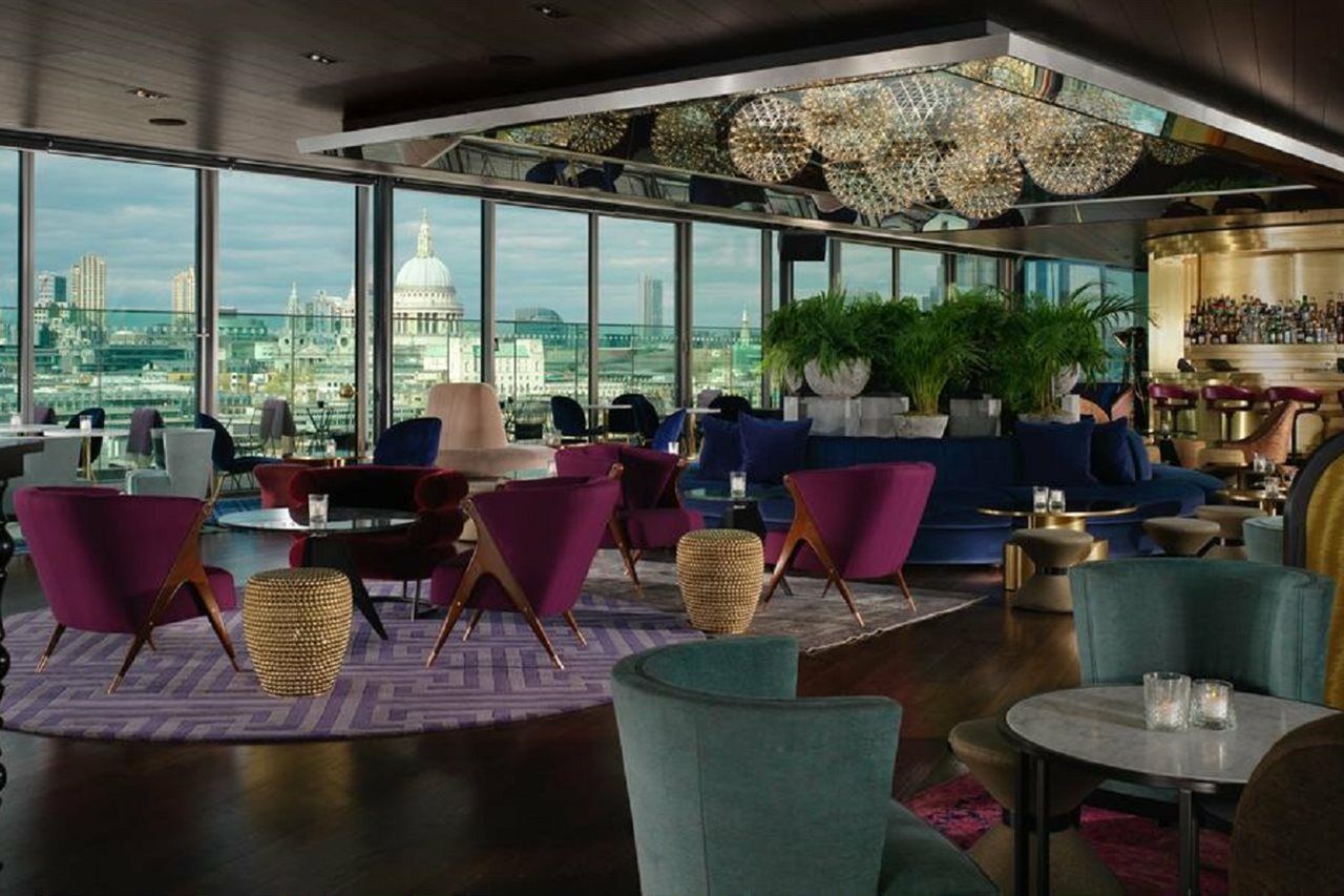 Sea Containers London Hotel Exterior photo The photo shows a stylish and contemporary interior of a lounge or bar. It features large windows that provide a panoramic view of the city, including a notable dome structure in the background, which appears to be St. Paul's Cathedral in London. 

T