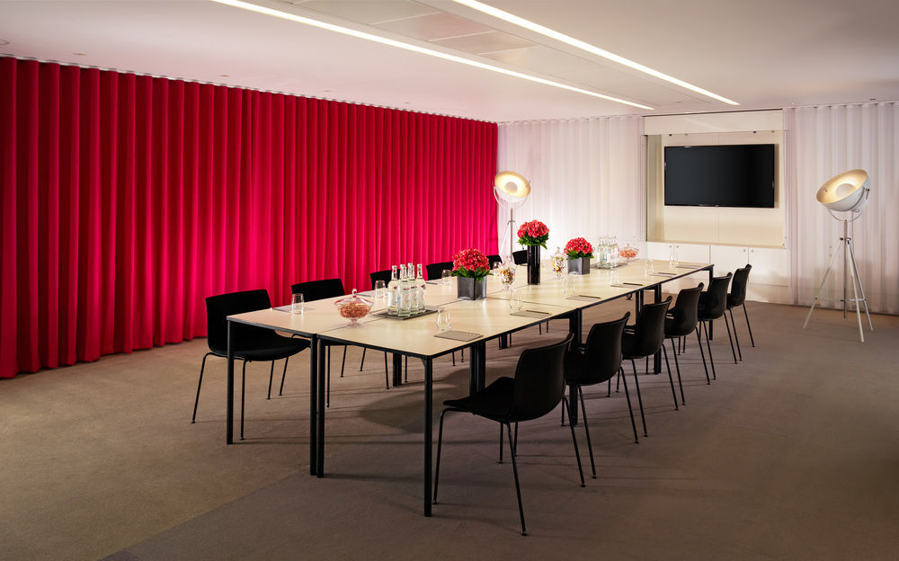 Sea Containers London Hotel Exterior photo The photo shows a modern conference room featuring a long table surrounded by black chairs. The table is set with glass bottles and small arrangements of flowers. Behind the table, there is a striking red curtain on one side and a white curtain on th