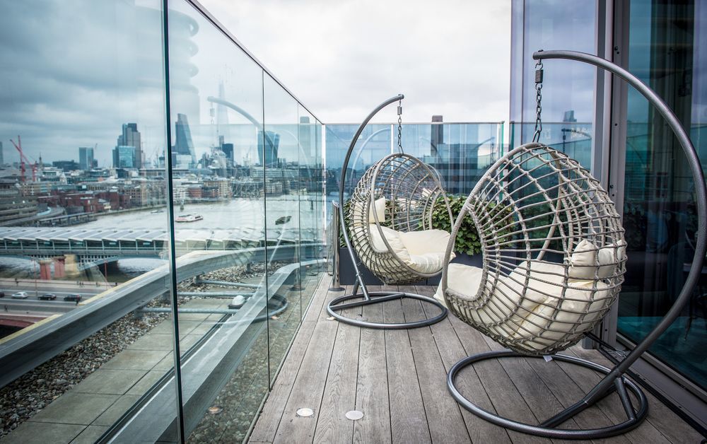 Sea Containers London Hotel Exterior photo The photo shows a stylish balcony with two hanging chairs designed in a circular shape, each suspended from a sleek metal frame. The chairs are made of woven material and have soft cushions for comfort. The balcony features a wooden floor and a glass