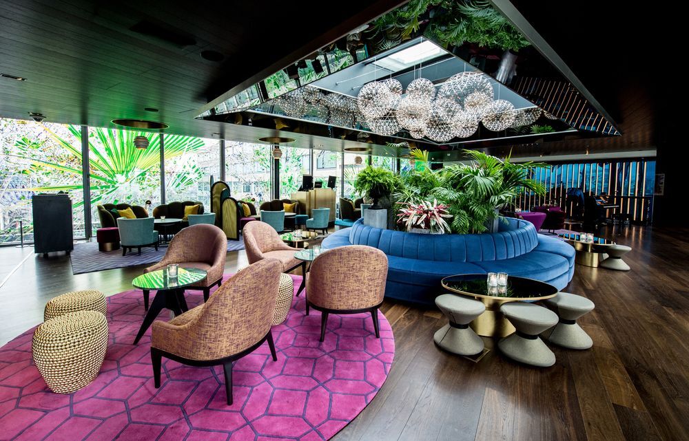 Sea Containers London Hotel Exterior photo The photo shows a modern and stylish lounge area. It features an elegant design with a mix of seating options, including comfortable armchairs and a large circular blue couch. The floor is covered with a vibrant pink rug. The space is adorned with lu